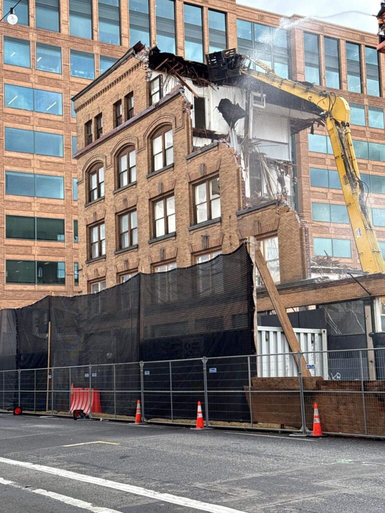 A photo of the Governor Building in Portland, Oregon being demolished by a yellow crane