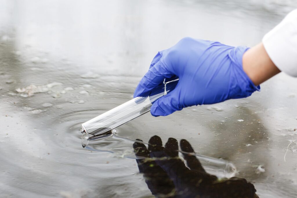 Hand with blue glove collects a water sample with a test tube